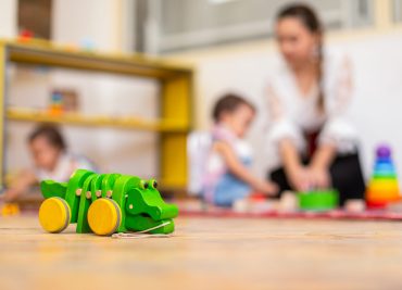 Closeup of wooden crocodile toy and kids playing with toys in the background in kindergarten