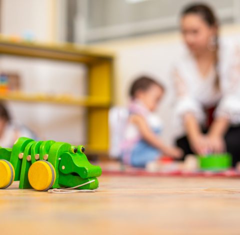 Closeup of wooden crocodile toy and kids playing with toys in the background in kindergarten